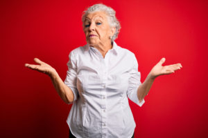 Senior woman in front of red background shrugging 
